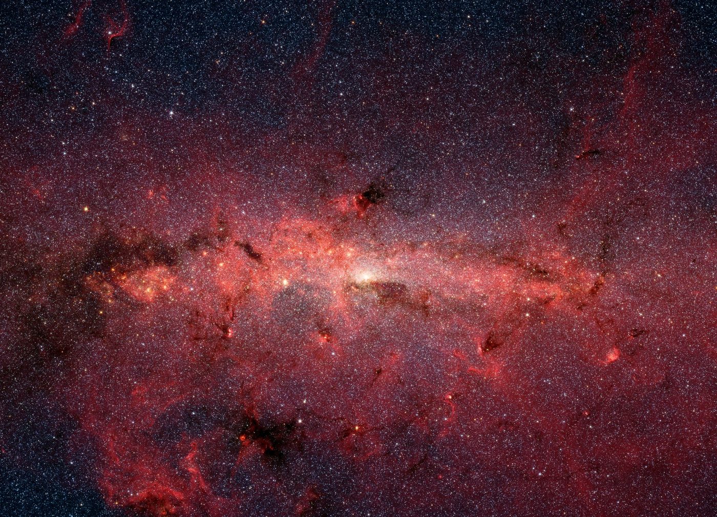 Spitzer Space Telescope infrared mosaic of the Galactic Center region showing dense star fields and glowing dust clouds.